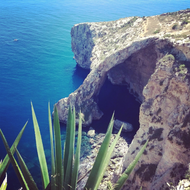 Felsige Steilküste mit Meeresgrotte, türkisfarbenes Wasser und grüne Pflanzen