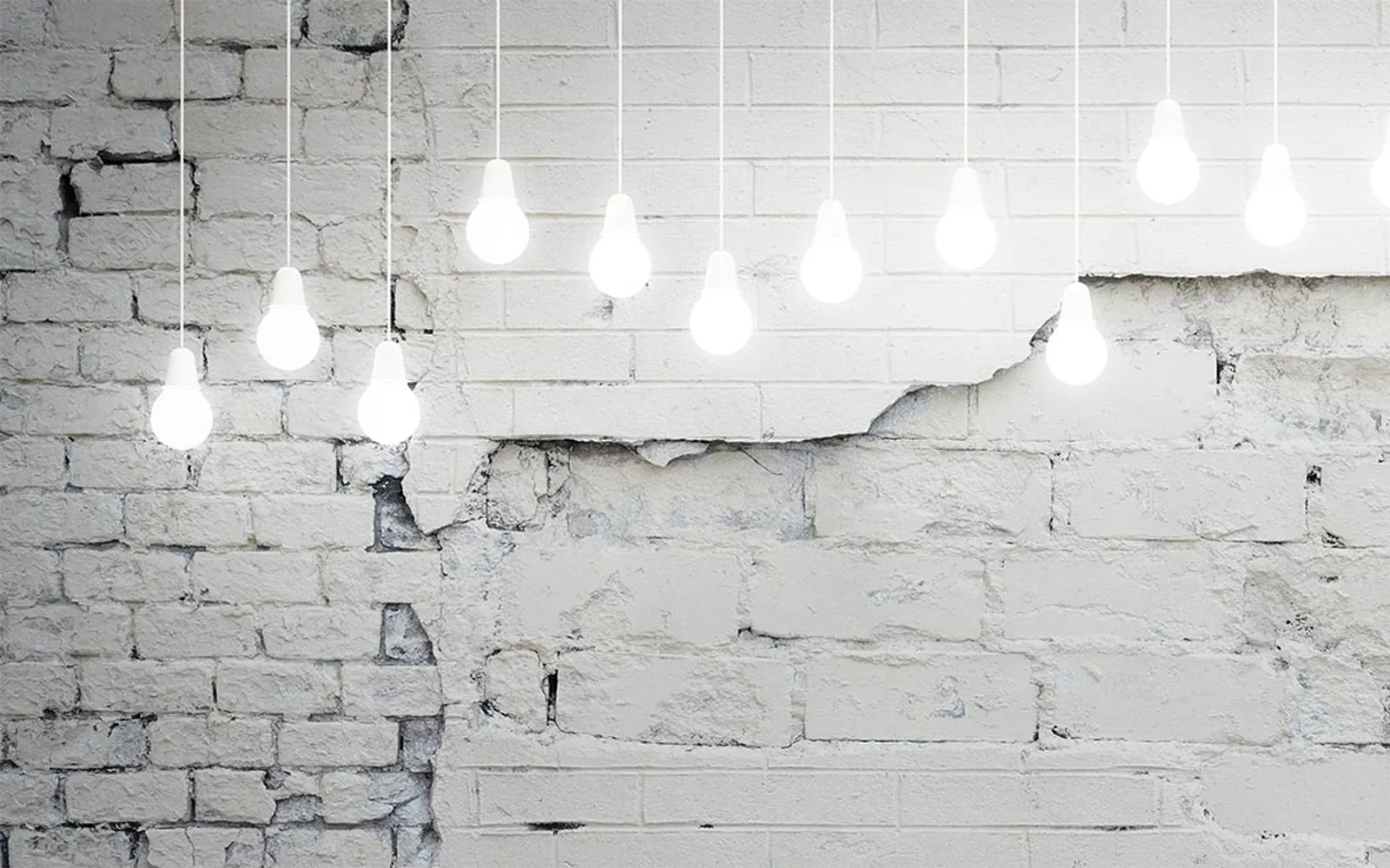 Row of warm glowing bare light bulbs hanging in front of a white painted brick wall, soft cozy indoor light
